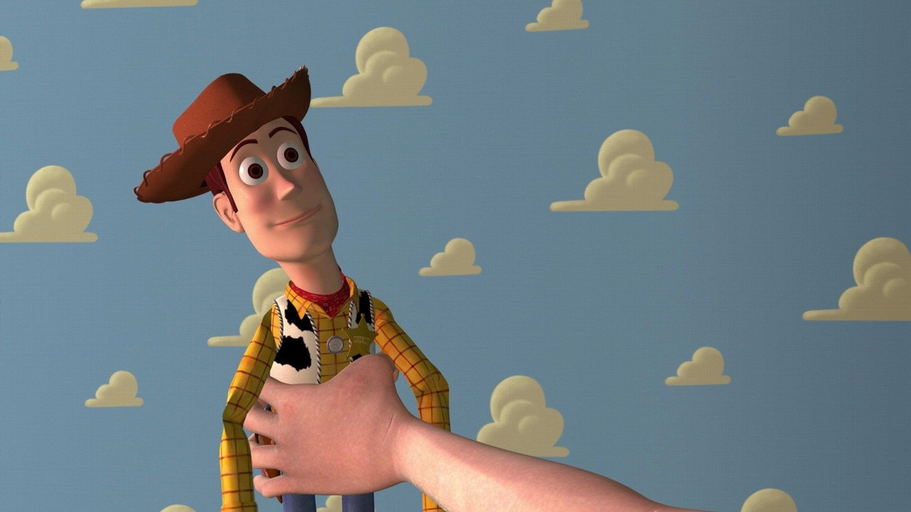 A second scene from the pack: Woody held up by a hand in front of a cloud-patterned wall.